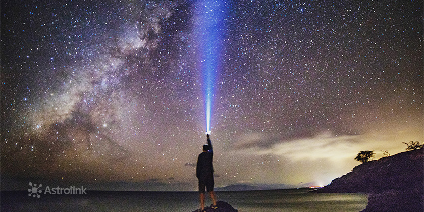 homem apontando lanterna azul para céu estrelado