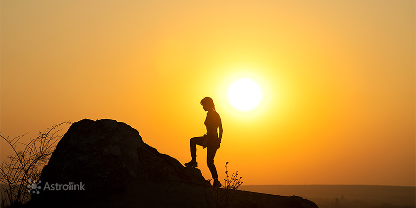 pessoa subindo montanha com por do sol ao fundo